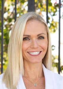 blond woman with a smile on her face standing in front of a fence