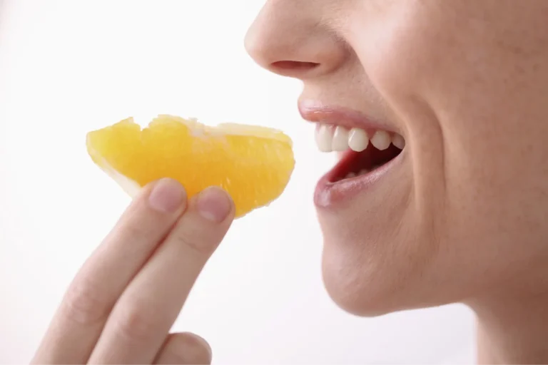 woman eating a piece of orange with her mouth open