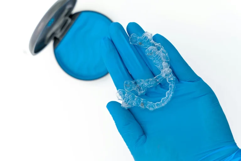 someone wearing blue gloves holding a clear plastic retainer