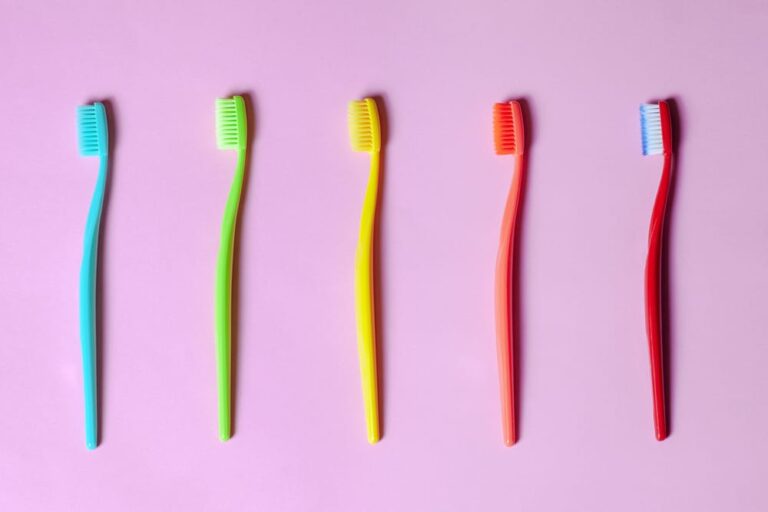 four different colored toothbrushes lined up on a pink surface