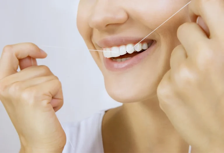 smiling woman holding a toothbrush and thread to her teeth