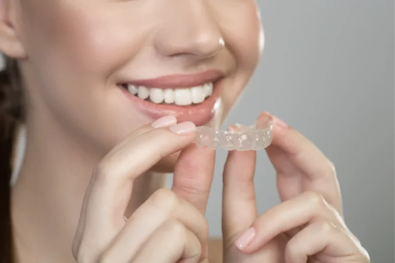 smiling woman holding a clear plastic retainer in front of her teeth