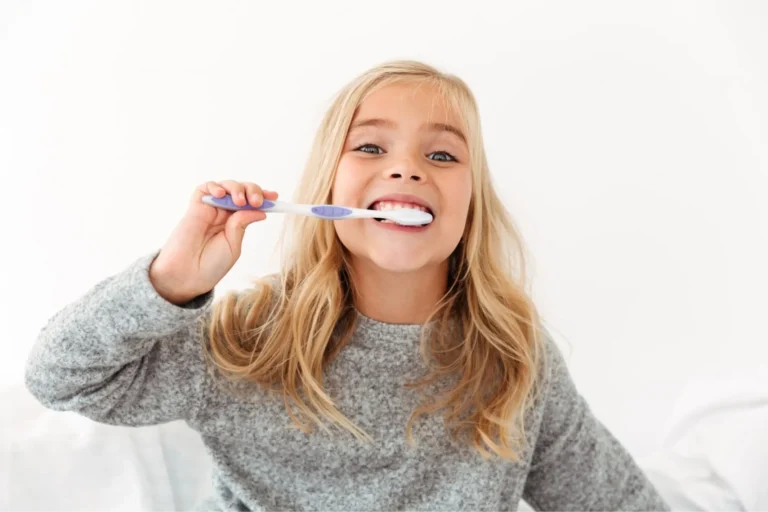 blonde girl brushing her teeth with a toothbrush in bed