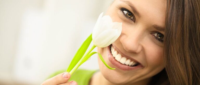 smiling woman holding a flower in front of her face