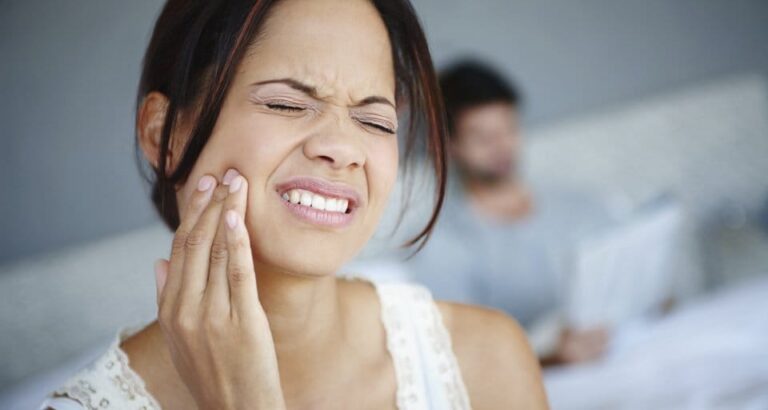 woman with toothache in bed with man in background