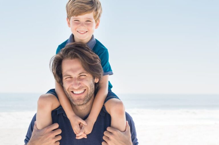 there is a man holding a boy on his shoulders on the beach