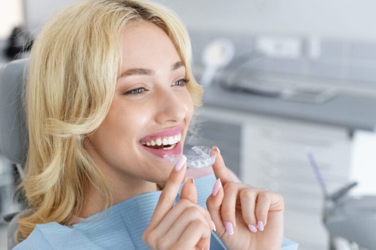 blond woman with braces holding in hand and smiling while sitting in dental chair