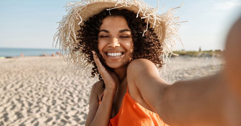 there is a woman in an orange dress and a straw hat on the beach