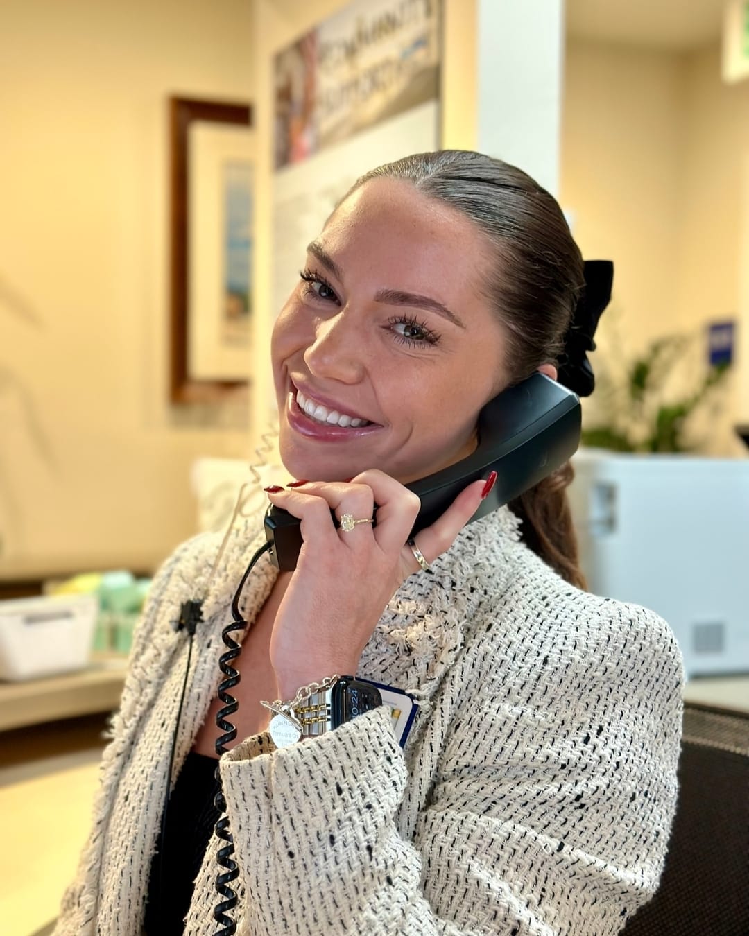 smiling woman talking on a phone in a room with a desk