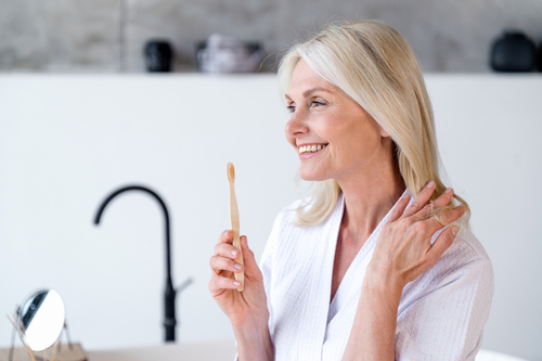 blond woman in white robe brushing her teeth in bathroom