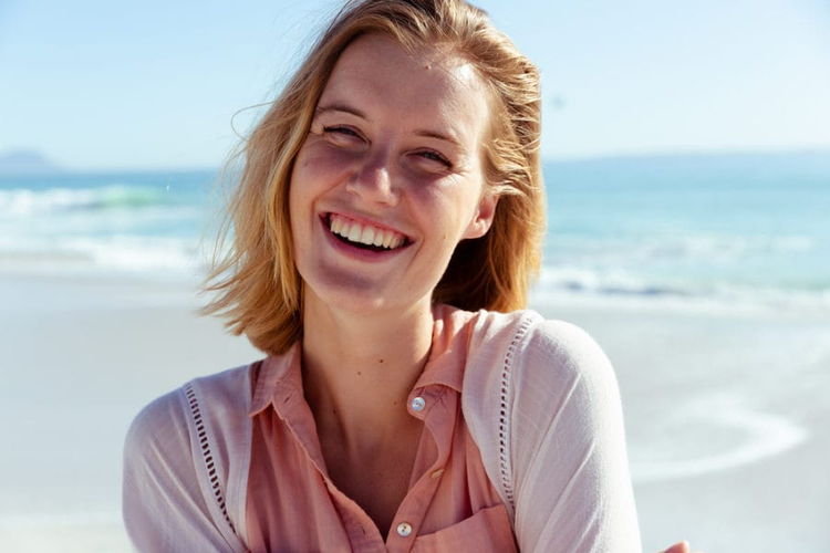 smiling woman with pink shirt on the beach with ocean in the background