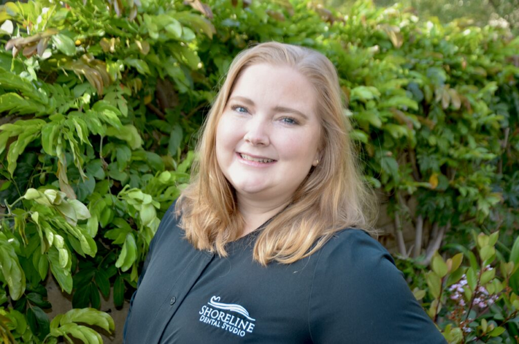 smiling woman in black shirt standing in front of a bush