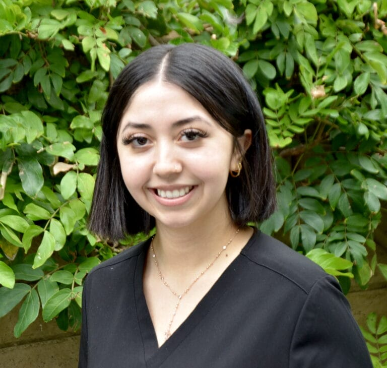 smiling woman in black top standing in front of a bush