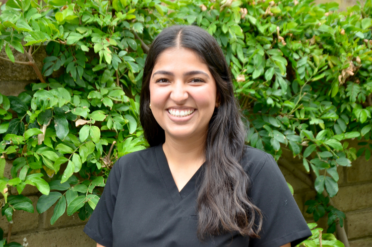 smiling woman in black shirt standing in front of a bush