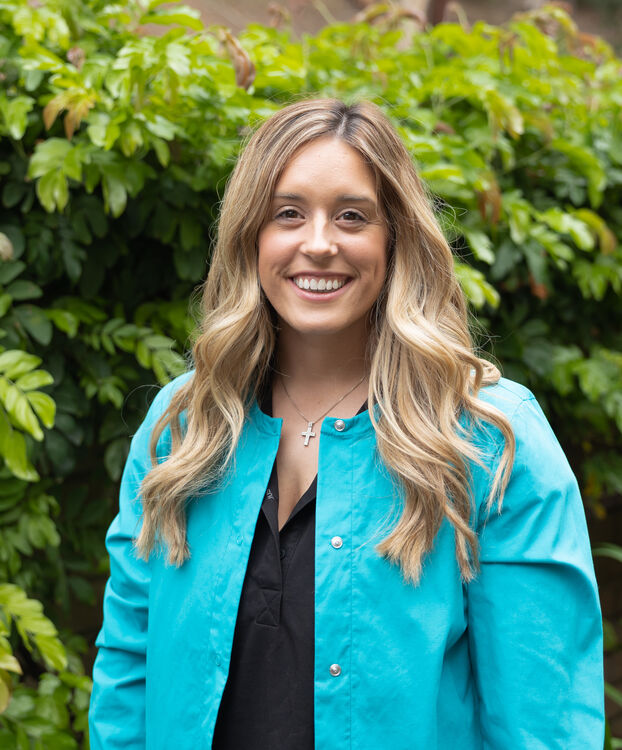 smiling woman in blue jacket standing in front of a bush