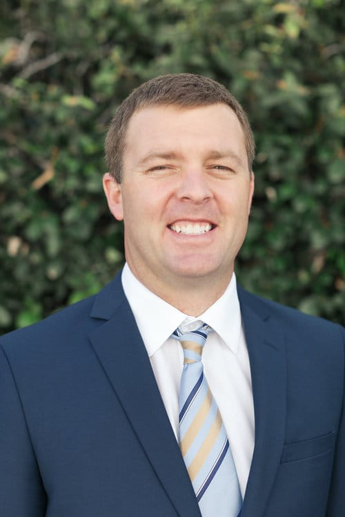 smiling man in a suit and tie standing in front of a bush