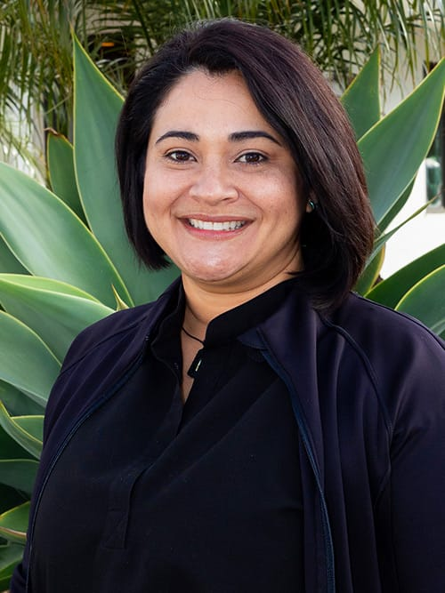 smiling woman in black shirt standing in front of a plant