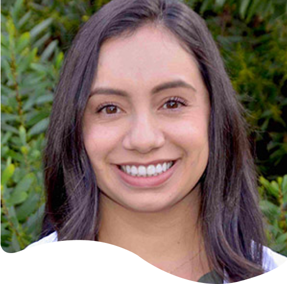 smiling woman with long dark hair and white shirt in front of bushes