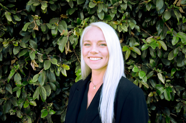 blond woman with white hair and black dress standing in front of a bush