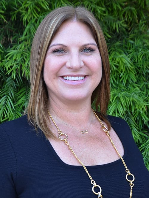 smiling woman in black top with gold chain necklace and black top