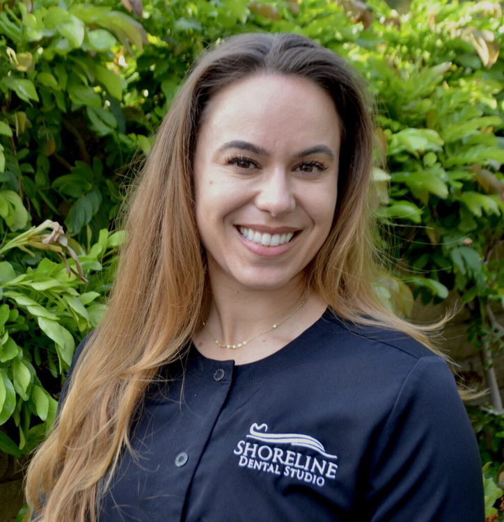 smiling woman in black shirt standing in front of bushes and trees