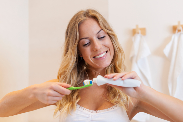 blonde woman brushing her teeth in the bathroom with a green toothbrush