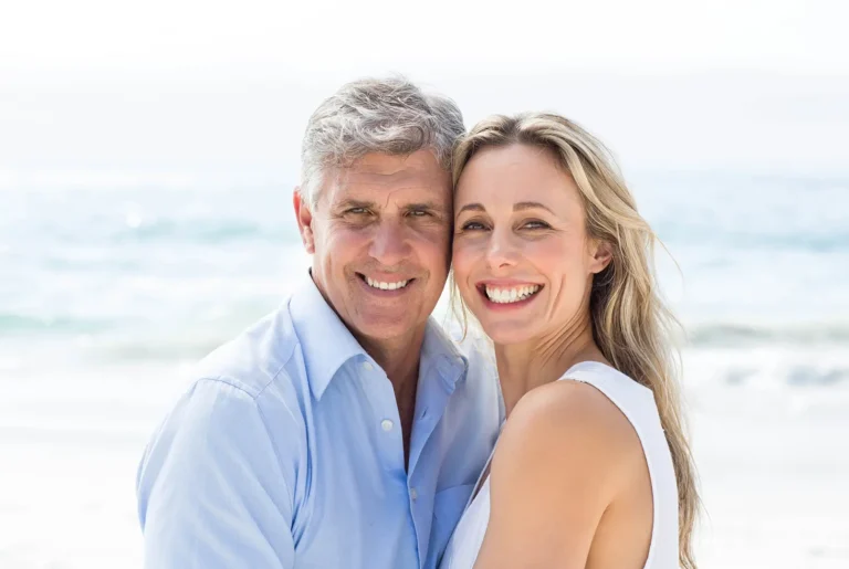 smiling couple embracing on the beach with ocean in the background