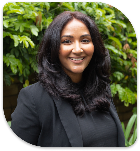 smiling woman in black jacket and black blazer standing in front of a bush