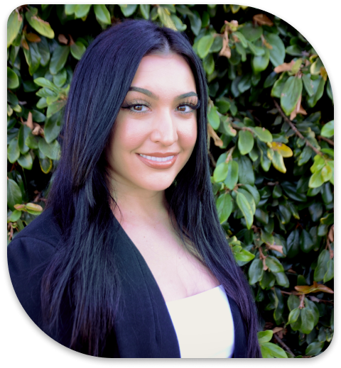 smiling woman with long black hair and white top in front of a bush