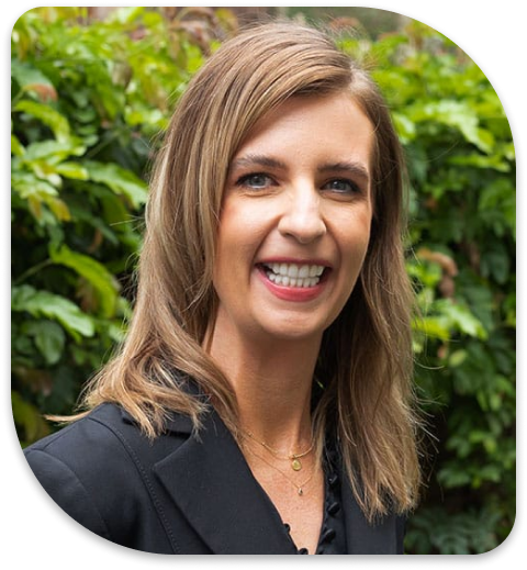 smiling woman with long hair and black blazer in front of bushes