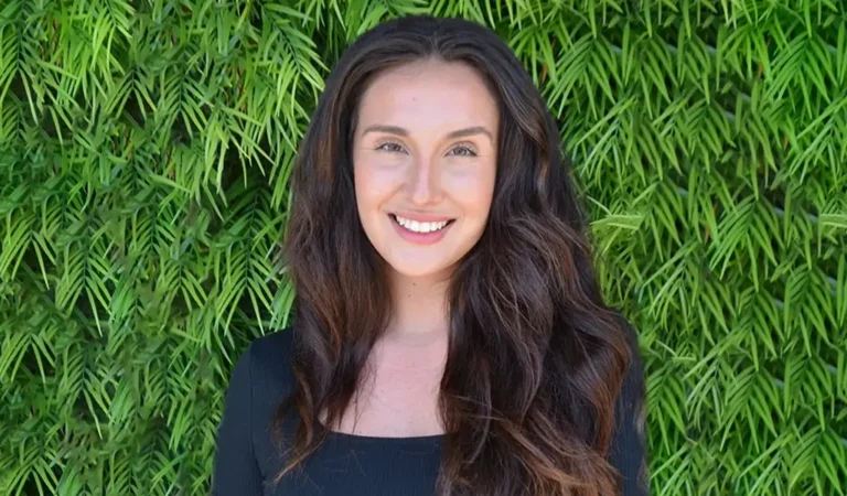 smiling woman with long dark hair and black top standing in front of a green wall