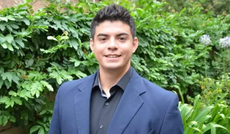 arafed man in a blue suit and black shirt standing in front of a bush