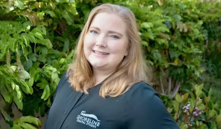 smiling woman in black shirt standing in front of a bush