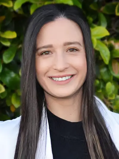 a woman with long black hair and a white jacket smiles