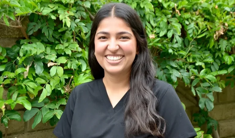 smiling woman in black shirt standing in front of a bush