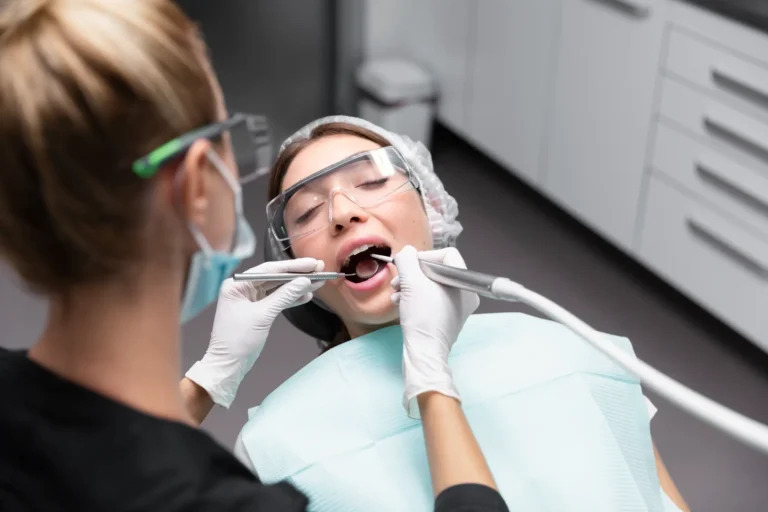 woman with glasses on her face getting her teeth brushed by a dentist