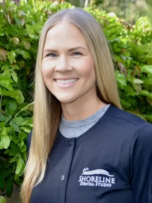 a woman in a black jacket standing in front of a bush