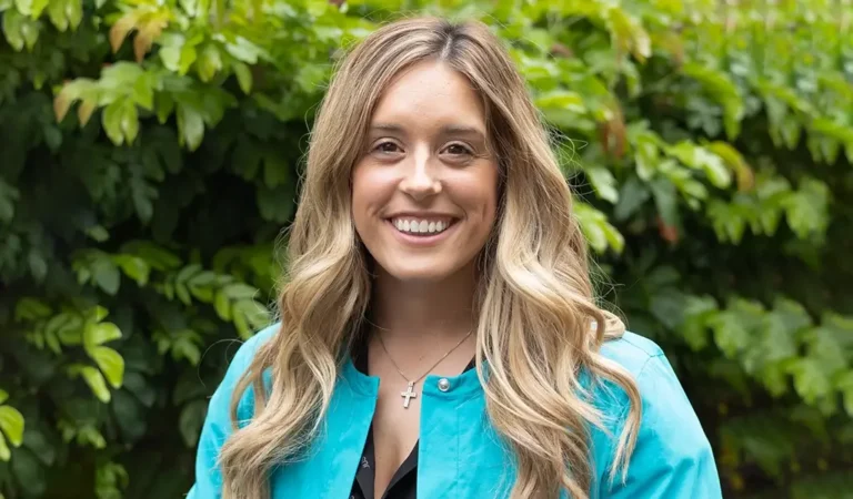 smiling woman in blue jacket standing in front of a bush