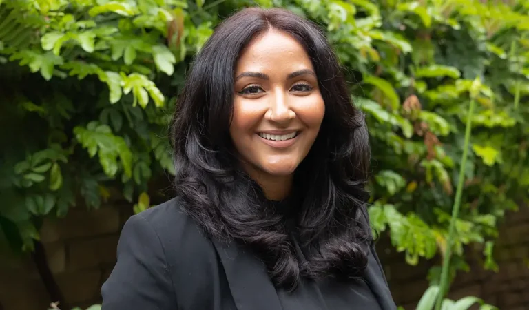 smiling woman in black jacket standing in front of a bush