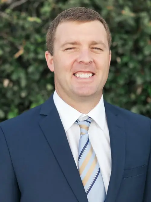 arafed man in a suit and tie smiling in front of a bush