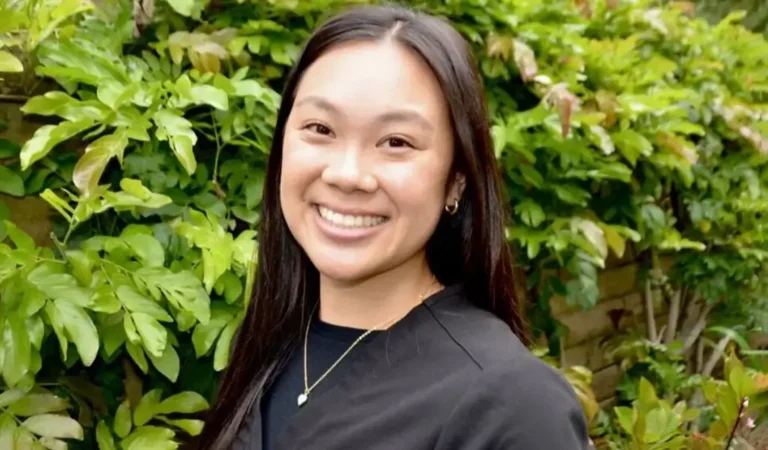 smiling woman in black shirt standing in front of a bush