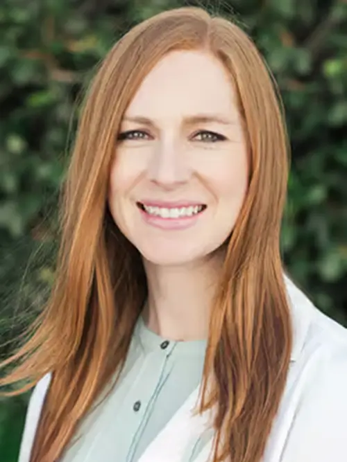 a woman with long red hair and a white coat smiles at the camera