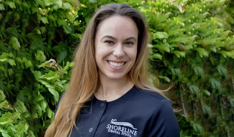 smiling woman in black baseball uniform standing in front of bushes