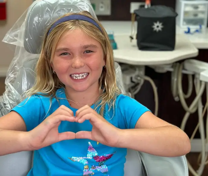 arafed girl sitting in a chair making a heart with her hands