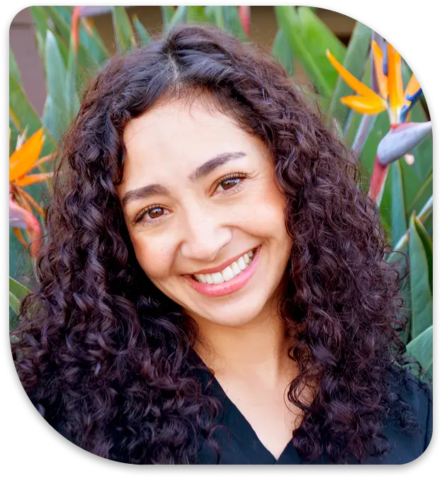 smiling woman with curly hair and a black shirt in front of a flower