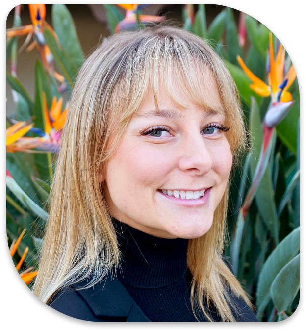 smiling woman with blonde hair and black turtle neck sweater in front of flowers